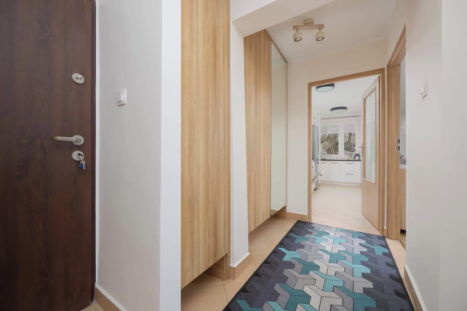 A hallway with a mirror, a blue rug, and wooden doors leading to different areas of the apartment, making the space feel more open.