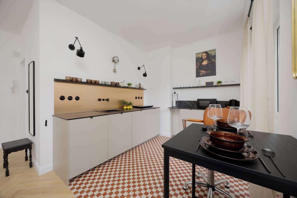 A small but modern kitchen with white cabinets, black countertops, and warm lighting, part of an open living concept.