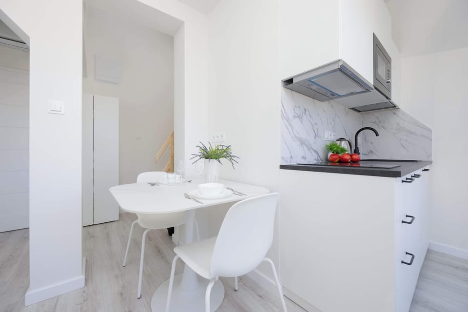 A small dining nook with a white round table, two chairs, and a nearby kitchenette.