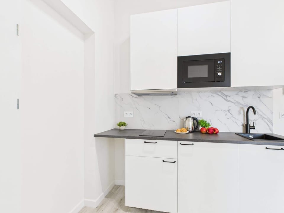 A compact white kitchen with modern appliances and fresh fruit on the counter. Minimalist and clean, perfect for easy meal prep.