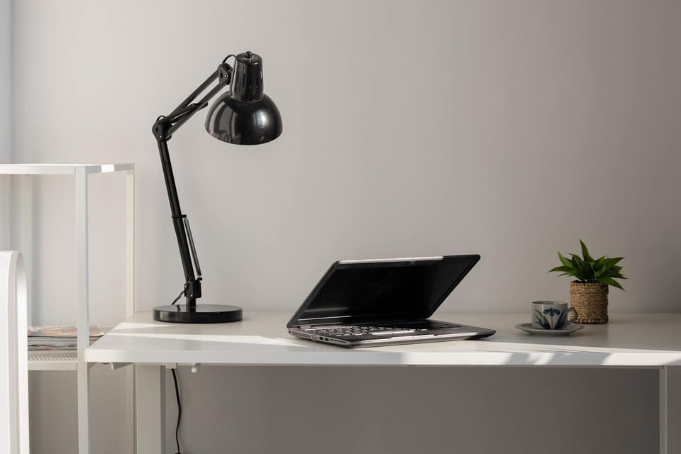 A compact home office with a sleek desk, adjustable lamp, and lush indoor plant, bathed in natural light from the window.