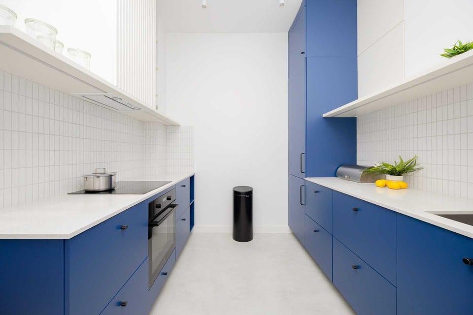 A stunning kitchen design featuring deep navy blue cabinets with brass handles, a pristine white tiled backsplash, and open shelving for an organized and stylish look. Ideal for cooking enthusiasts seeking both functionality and aesthetics.