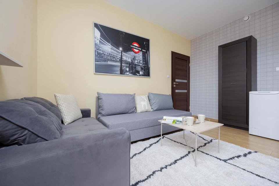 A spacious living room with a gray sofa, white rug, and light yellow walls. Large windows provide ample natural light.