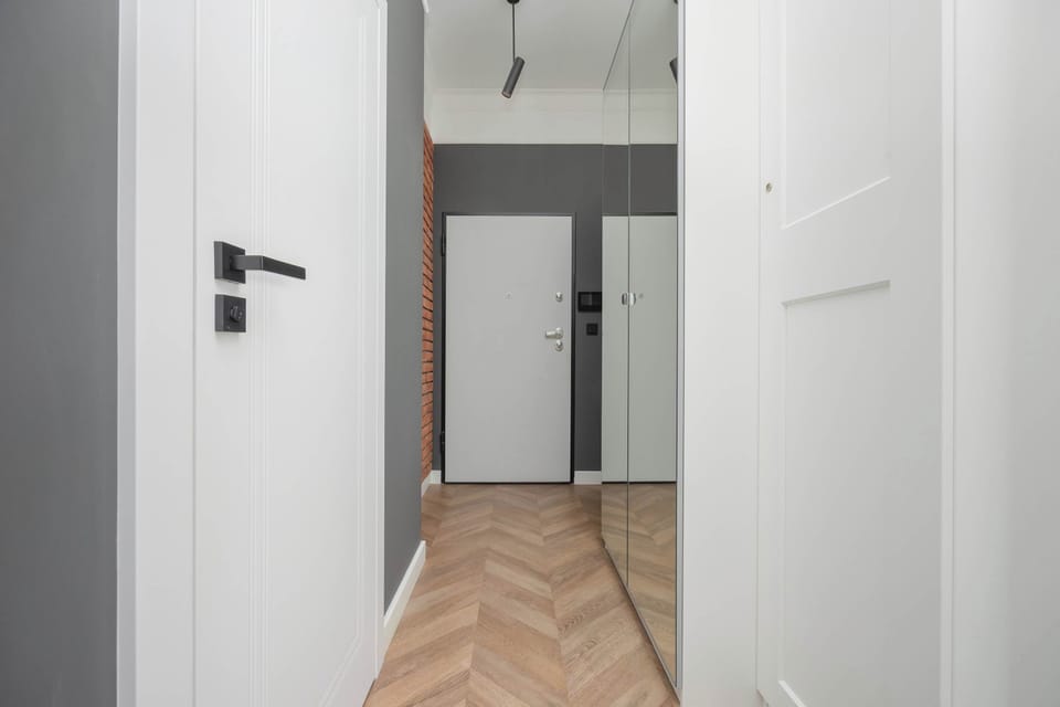 A corridor with white walls and doors, accented by light wood flooring and simple modern design.