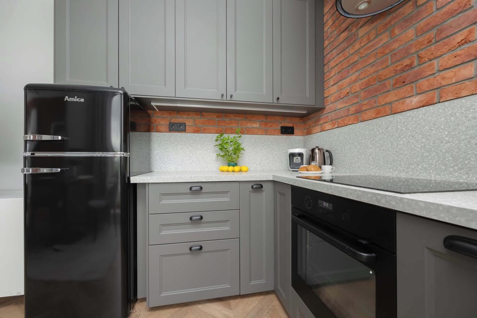 A compact kitchen corner featuring a black refrigerator, microwave, gray cabinets, and exposed brick backsplash.