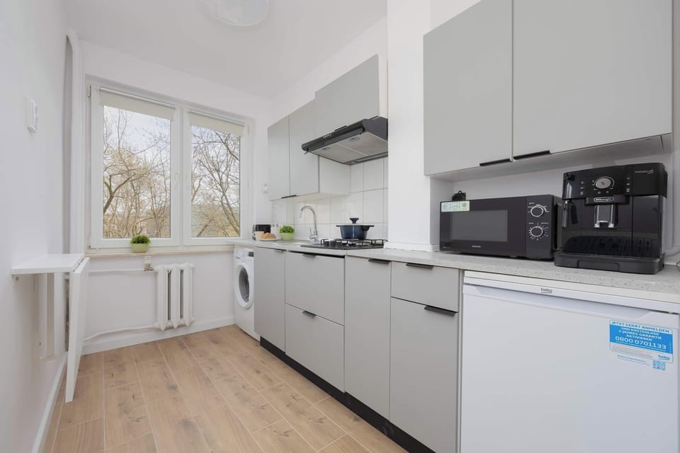 A white, fully equipped kitchen with modern appliances and a view outside.

