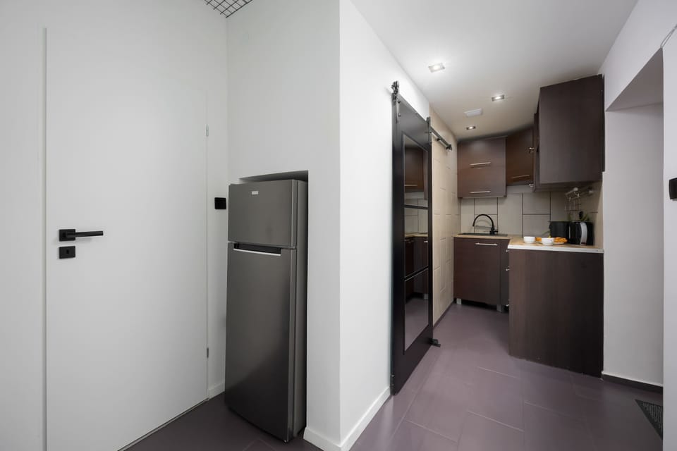 A hallway leading to the kitchen, showing a modern, minimalistic entrance with a refrigerator.