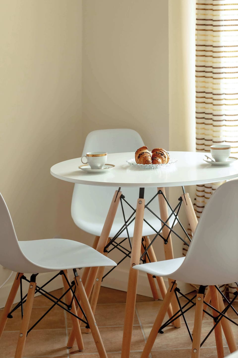 A dining area with a small round table and two chairs, set next to a large window with soft curtains, creating a cozy breakfast nook.
