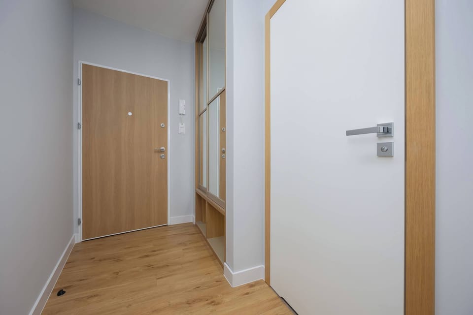 A hallway leading to various rooms in the apartment. The neutral-toned walls and wooden flooring give it a sleek appearance.
