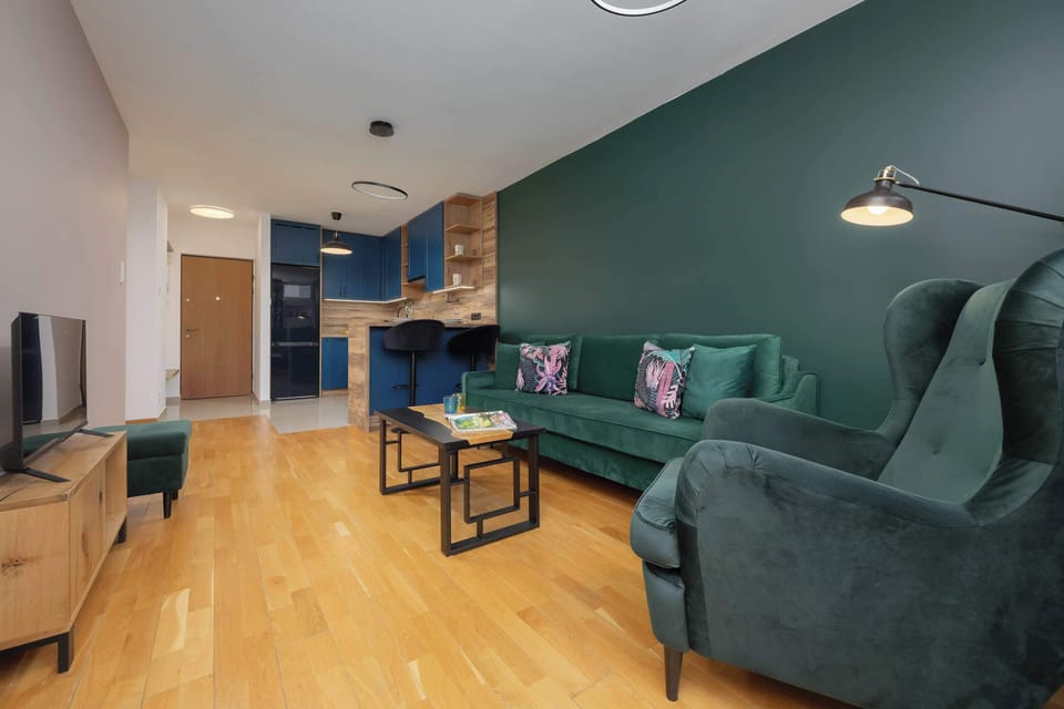 A cozy living room with a green couch, a TV, and a minimalistic style. It is designed to be both functional and inviting.