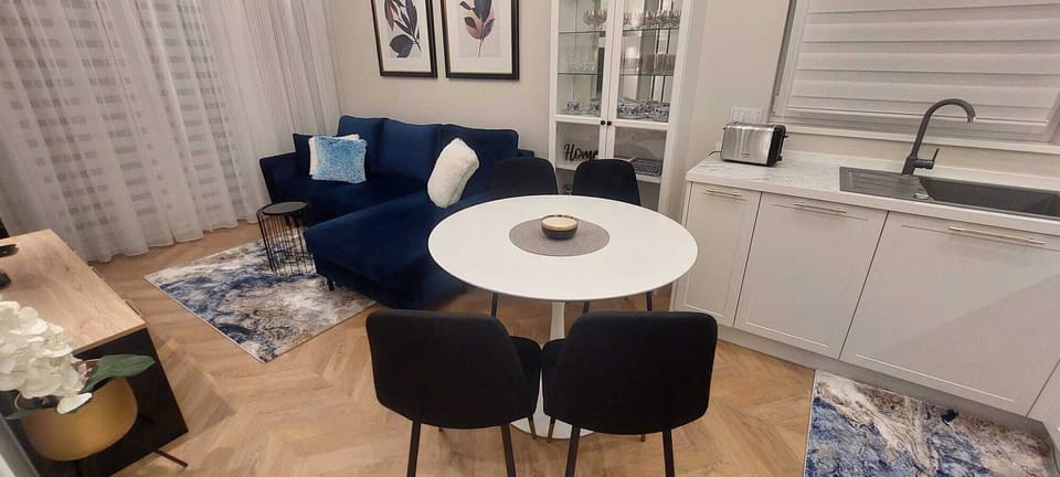 Living room with navy sofa, white table, and kitchenette with white cabinets creates a modern, functional space with elegant accents.