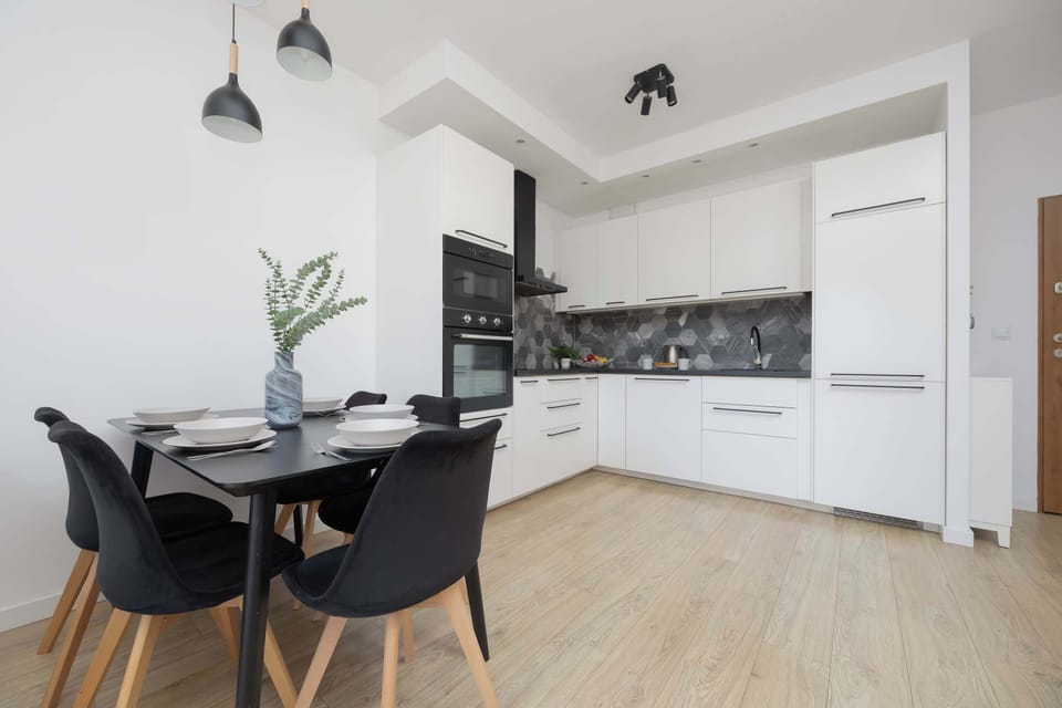 A modern open-plan kitchen and dining area with white cabinetry and a sleek black dining table with chairs.