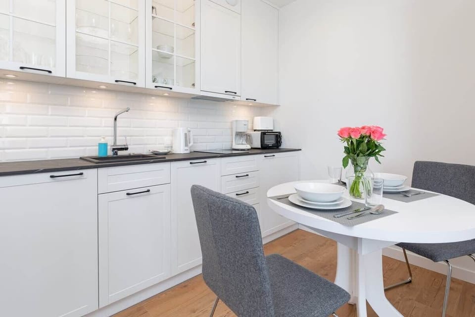A compact kitchen with white cabinets, a microwave, and a small dining area adjacent to it.