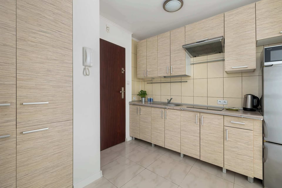 A kitchen with wood-textured cabinets, a silver refrigerator, and tiled walls next to a dark wooden entrance door.