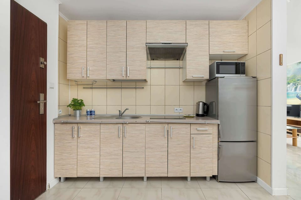 A small kitchen area with beige cabinetry, a countertop workspace, and a silver refrigerator by a wooden door.


