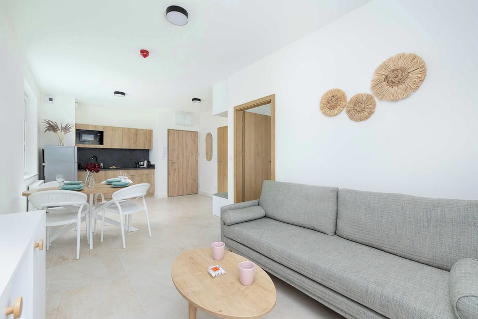 Living room, featuring a gray sofa, coffee table, and a light wood and white color scheme. It looks out towards the kitchen, emphasizing an open layout that feels connected and spacious.