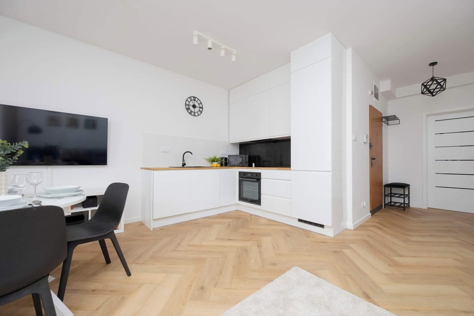 A wide-angle shot of the kitchen featuring white cabinetry, a wooden countertop, and integrated appliances, with light wooden flooring matching the living room.