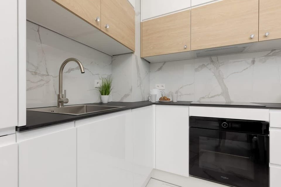 A minimalist kitchen with white and wooden cabinets, a sink, and a black countertop.