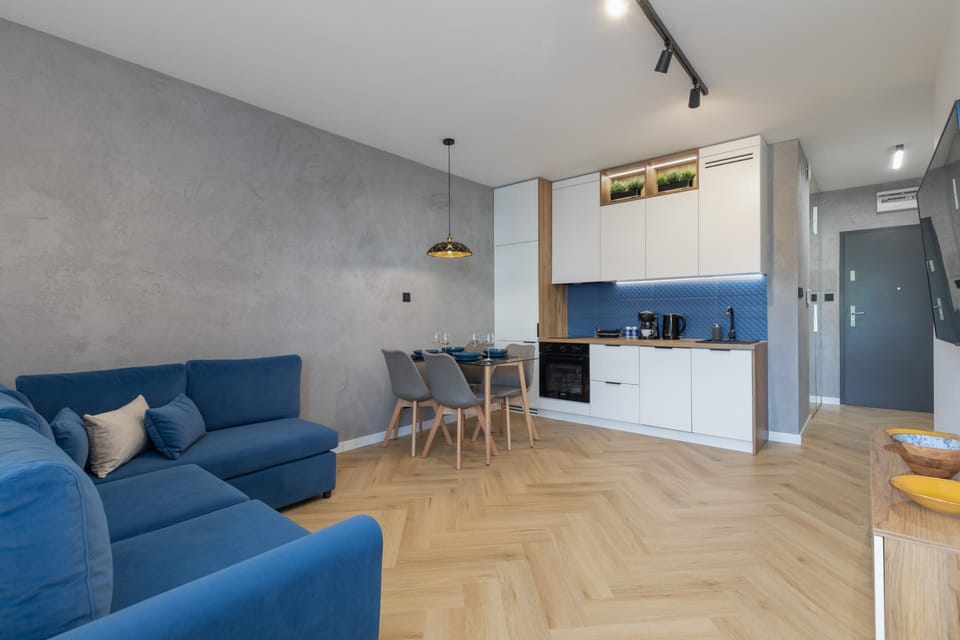 A spacious living and kitchen area with sleek wooden floors, blue furniture, and a minimalist design.
