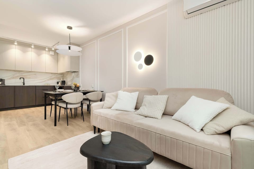 An inviting living room with a white sofa and large windows that bring in plenty of sunlight. A wall-mounted TV completes the entertainment setup.