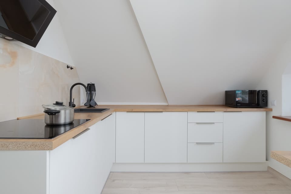 Kitchen with white cabinets with wooden countertop, induction stove, microwave oven and dishwasher. 
