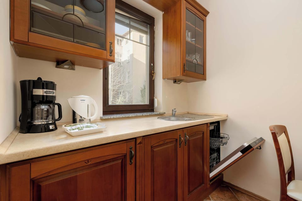 There is a coffee machine and an electric kettle on the bright countertop. There is a built-in dishwasher in the cupboard.