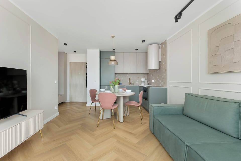 Cozy living room with a green sofa, TV and kitchenette with dining area.