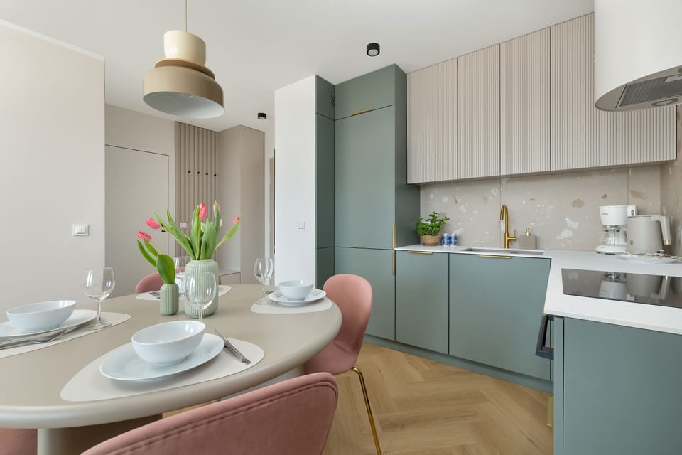 Dining room with round table, pink chairs and kitchenette with pastel accents.
