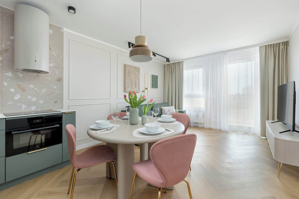 Living room and dining area with a table, pink chairs and a minimalist kitchen in shades of gray and white.