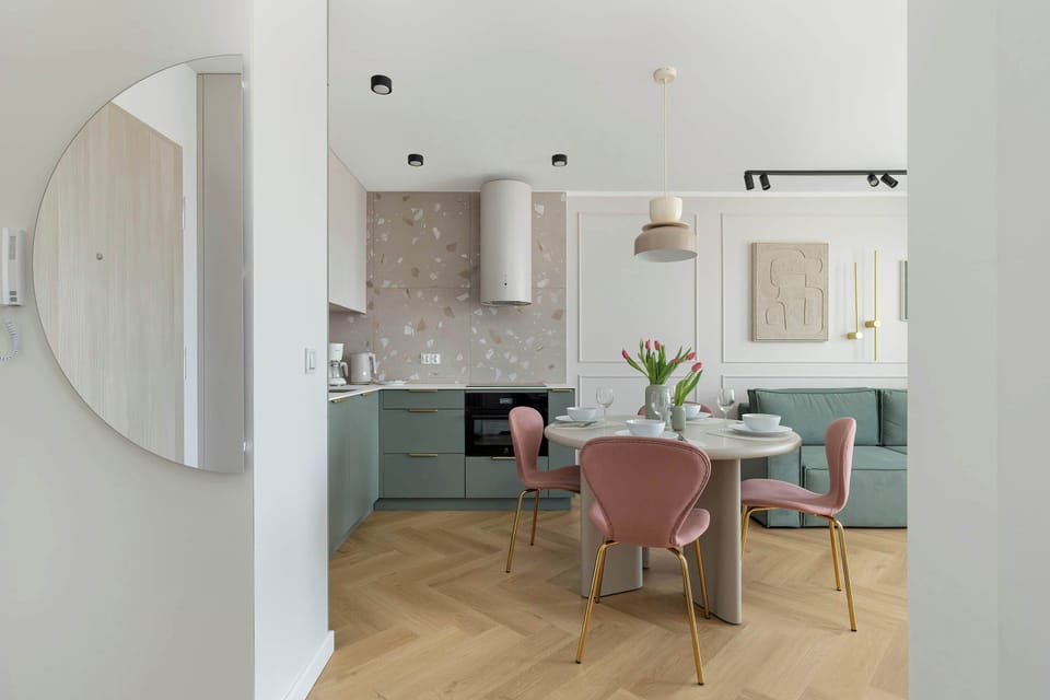 The view from the hallway to the living room with green sofa and kitchenette with table and chairs. The color scheme is bright and fresh.