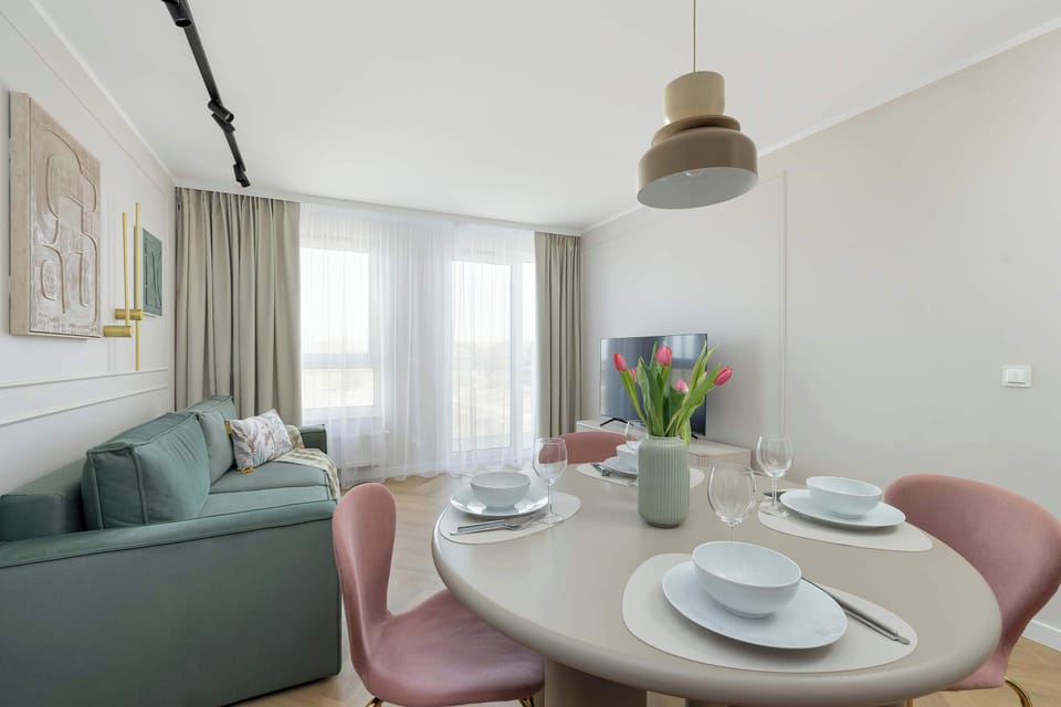 Cozy and modern living room with a green sofa, TV, round table and pink chairs.