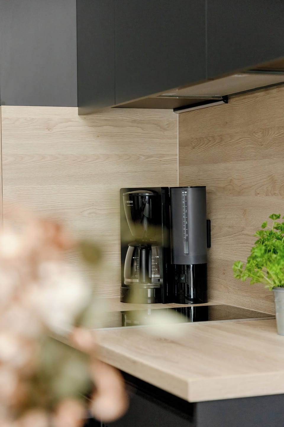 A close-up of a coffee setup on a wooden counter with a coffee machine and green plant beside it.