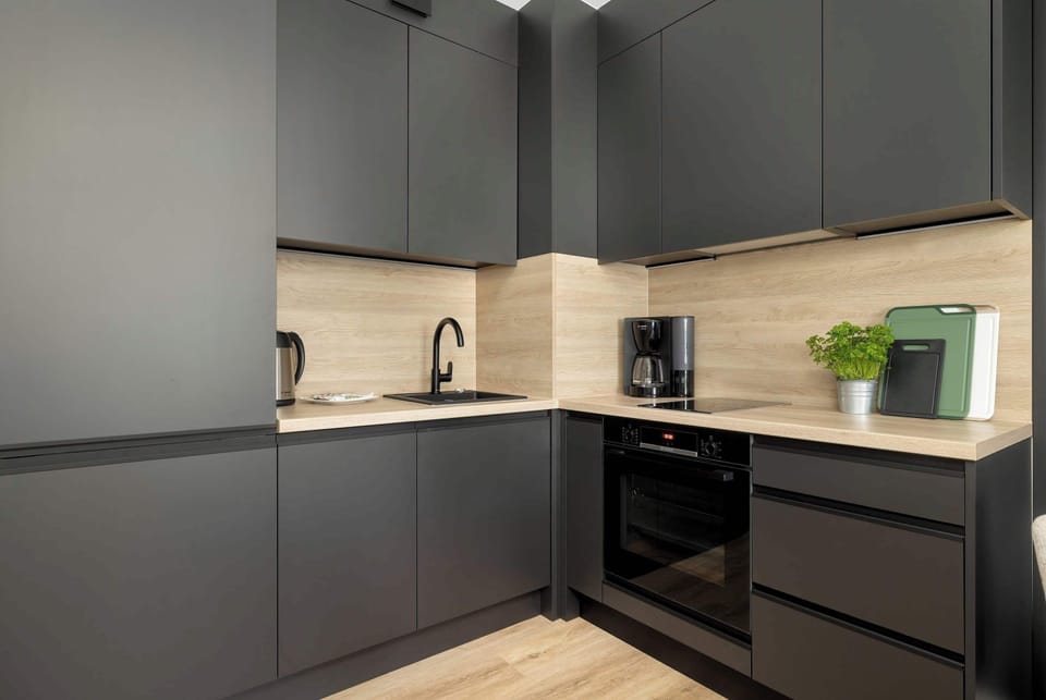 A compact yet functional kitchenette with matte black cabinets, light wood backsplash, and modern appliances