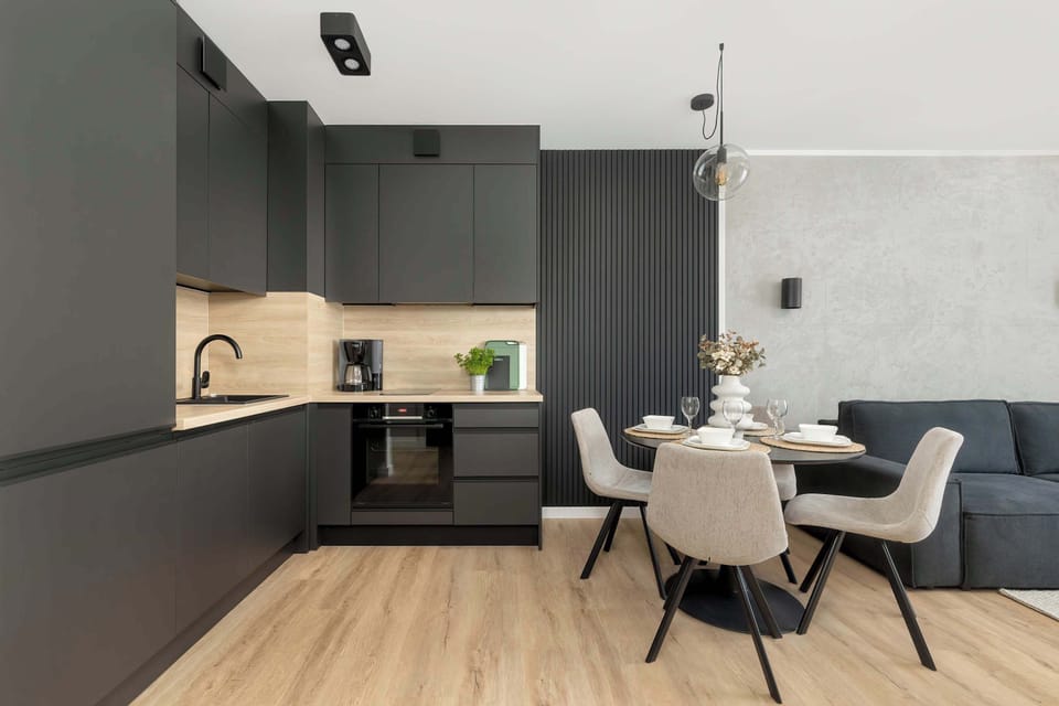 A modern open-plan kitchenette and dining area with black cabinetry, wooden accents, and a round table with four chairs.