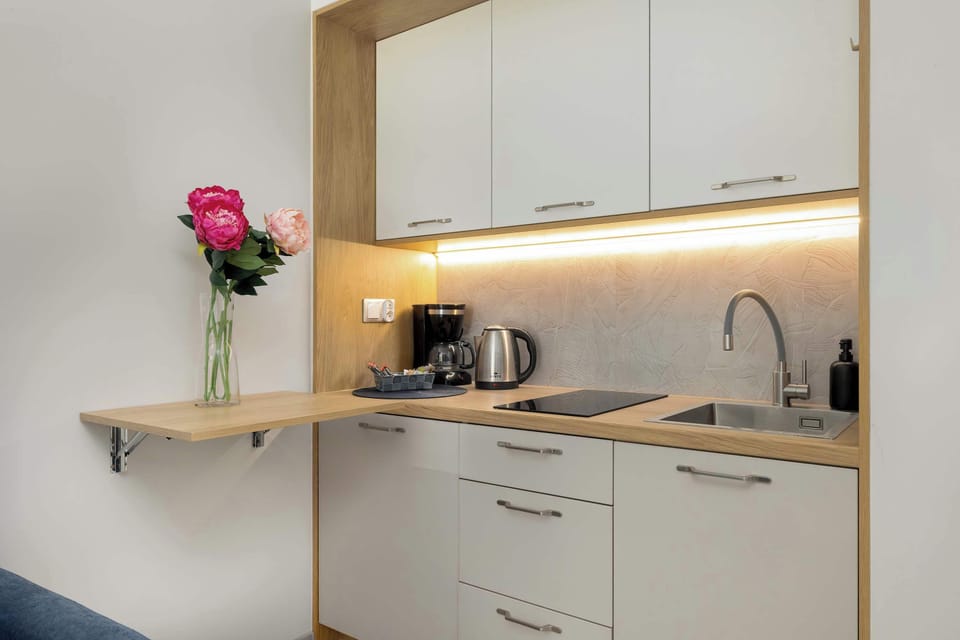 A compact kitchen with white cabinetry and wooden accents. Under-cabinet lighting illuminates the countertop. The design looks modern and efficient.