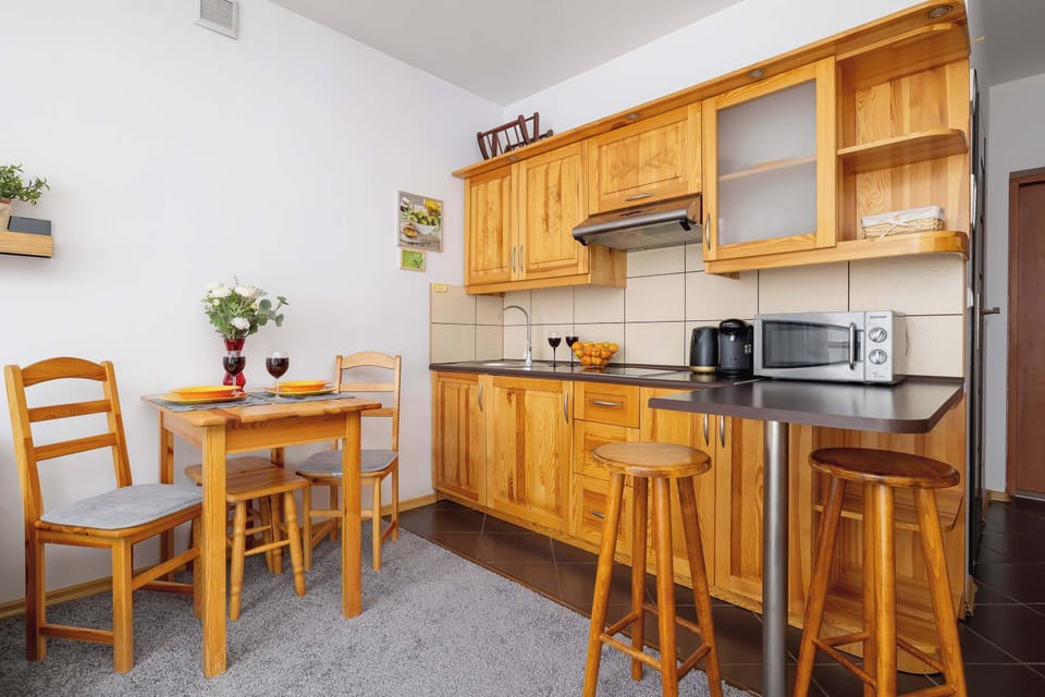 A wooden kitchen area is equipped with cabinets, a stove, a microwave, and a small dining table with two chairs. Warm lighting enhances the room's inviting atmosphere.