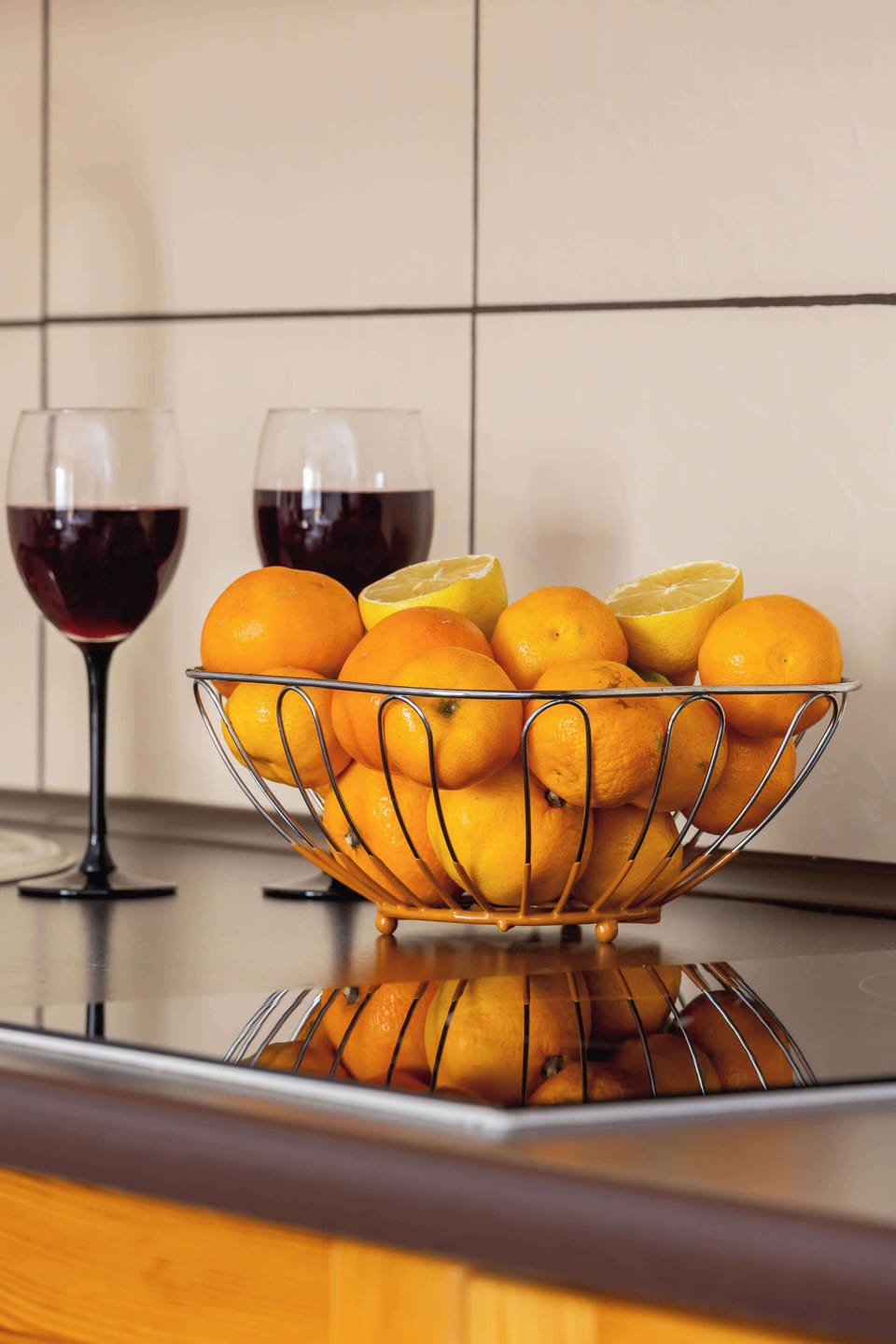 A wooden countertop features a bowl of fresh oranges and two wine glasses, creating a stylish and inviting atmosphere.