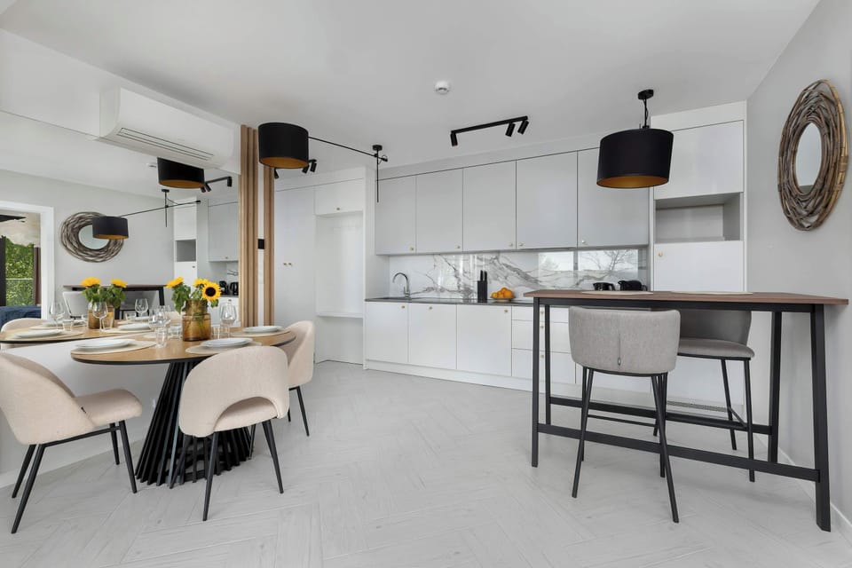 A spacious open-plan kitchen and dining area with sleek white cabinets. Black bar stools and pendant lights add a contemporary touch.