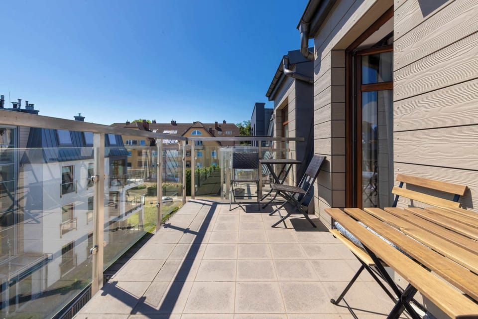 Sunny balcony with wooden flooring, outdoor furniture, and a city view.