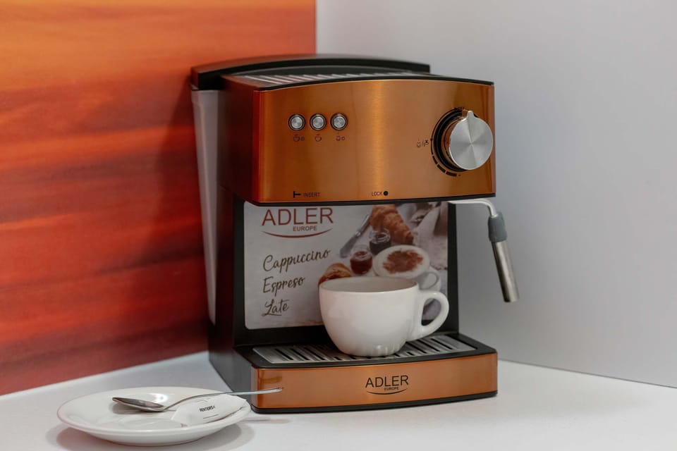 A sleek coffee station with a high-end coffee machine, a cup, and decorative details set against a bold orange backsplash.

