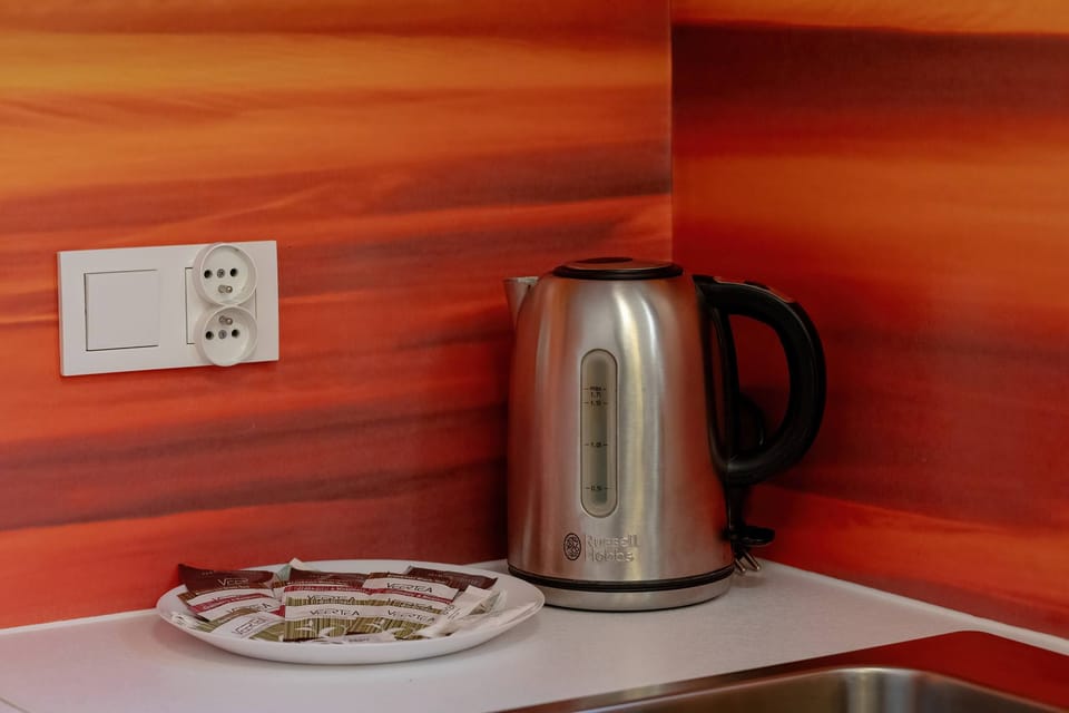 A kitchen corner with a stainless-steel kettle, a white tray, and an orange backsplash, blending convenience with modern design.







