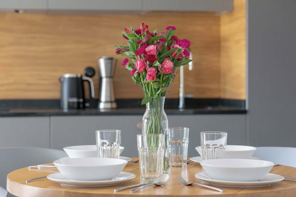 Table set for two with flowers, plates, and glasses, against a wooden kitchen background.
