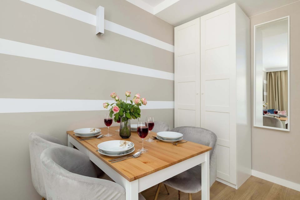 A breakfast nook with a small round table and two chairs, situated beside a striped wall. A bouquet of flowers brings a fresh touch to the space.