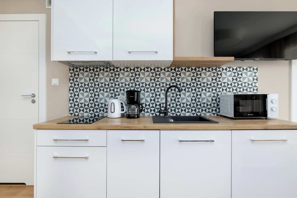 A wider view of the kitchen showing white cabinets, an electric stove, and small kitchen appliances. The backsplash adds a modern design element to the space.