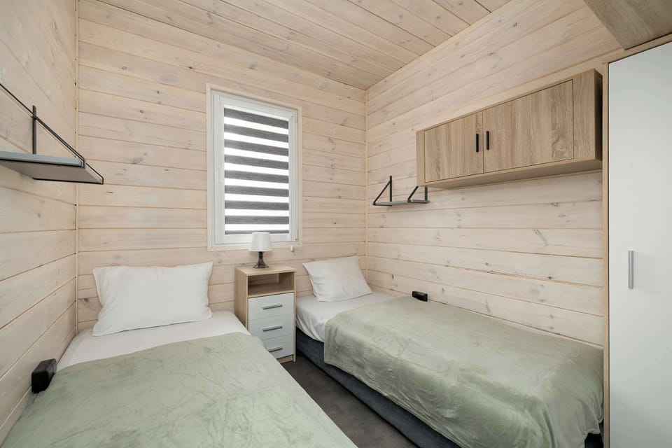 Bedroom with two single beds, a nightstand in between, and a window with blinds.