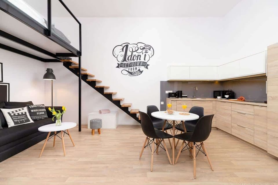 A loft-style bedroom area with a high ceiling, a dining table, and a staircase leading to the upper level.
