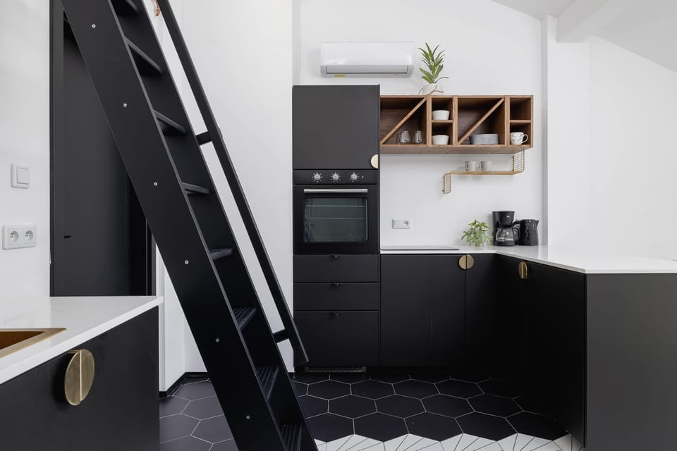 View of the kitchen and mezzanine stairs, showing black cabinetry and wooden shelves.