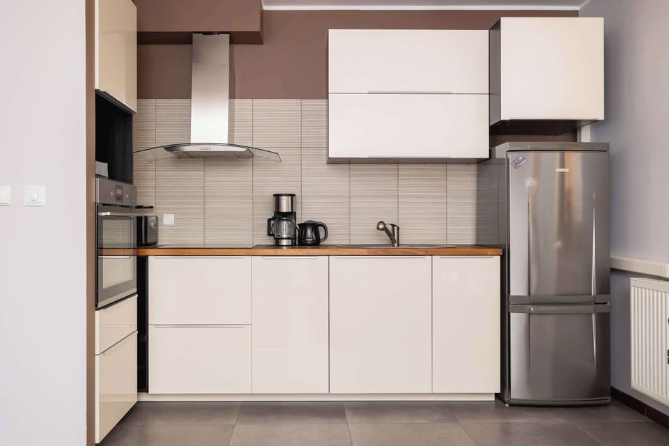 A kitchen with minimalist white cabinets, a stainless-steel refrigerator, and practical workspace.
