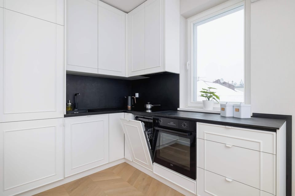 A well-equipped modern kitchenette with sleek white cabinets, black countertops, and a minimalist design. It’s paired with a dining area for casual meals or group dining.