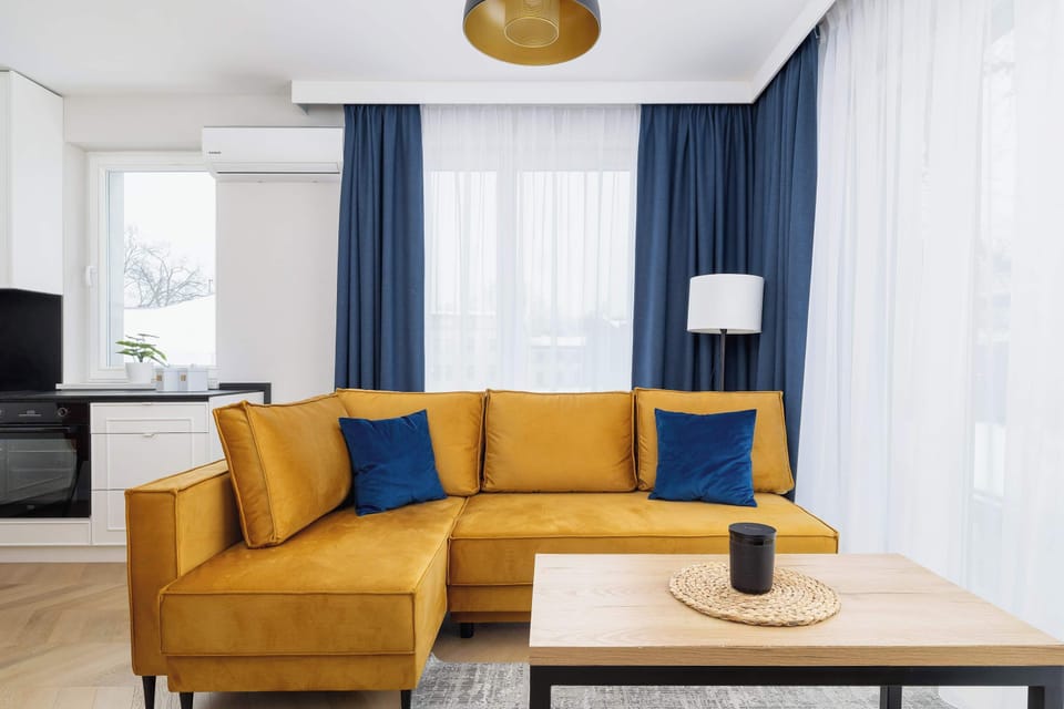 A vibrant living room and dining space combined, with a yellow sofa, coffee table, and a dining table with orange chairs. A perfect spot for social gatherings and comfort.